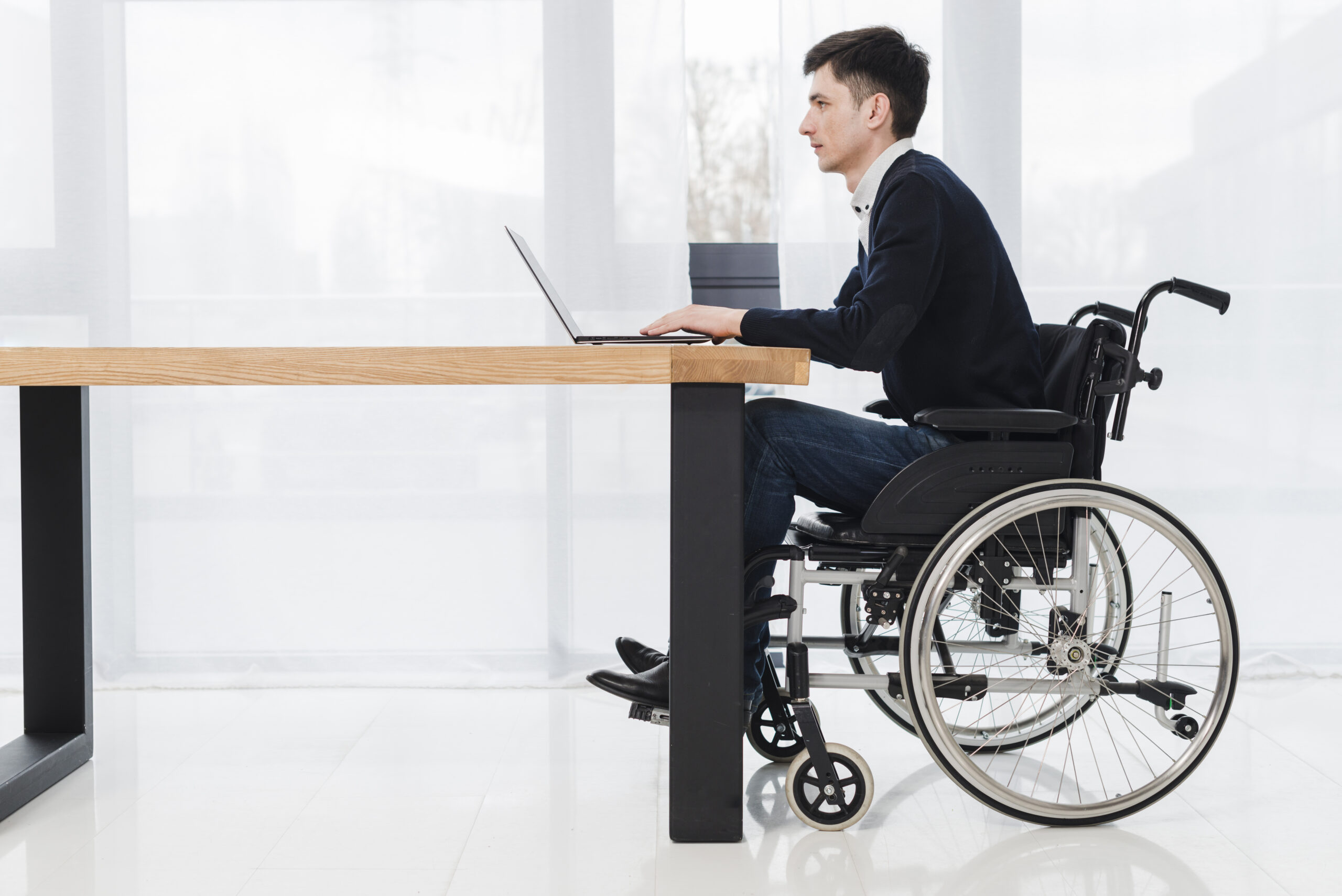 side-view-young-businessman-sitting-wheelchair-using-laptop-new-office
